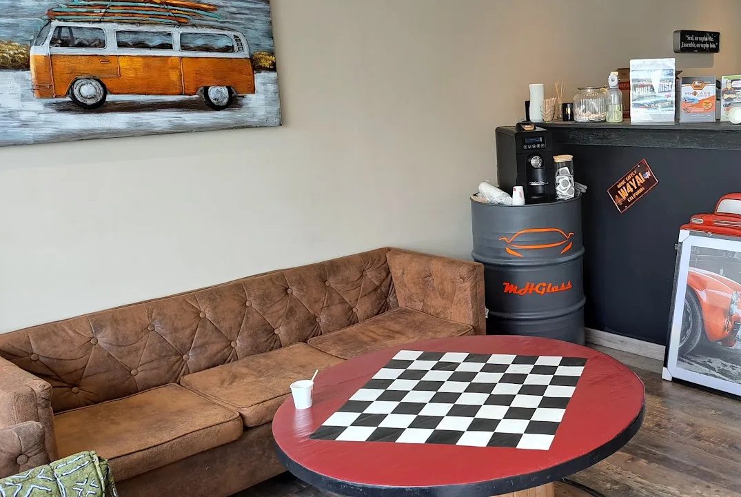 La salle d'attente de MH Glass : canapé en velours, table ronde rouge à damier, et un fût peint aux couleurs de l'atelier servant de station à café.