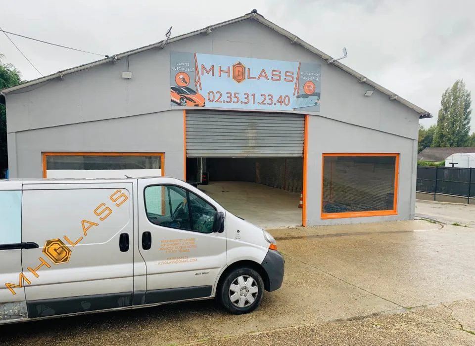 La façade de l'atelier MH Glass : l'enseigne orange, la travée ouverte et la camionnette de l'entreprise garée devant.